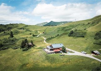 Eine ruhige Landschaft mit sanften Hügeln und einer kleinen Hütte. Der Himmel ist teilweise bewölkt und die Umgebung ist grün und einladend.