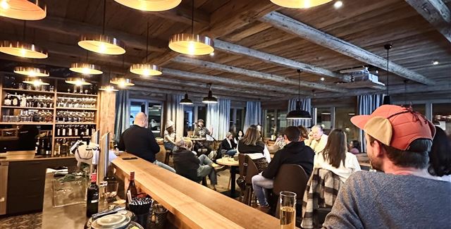 Eine gemütliche Bar mit Holzdekor und warmen Lichtern. Menschen genießen Getränke und unterhalten sich in einer einladenden Atmosphäre.