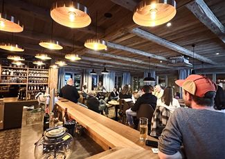 Eine gemütliche Bar mit Holzdekor und warmen Lichtern. Menschen genießen Getränke und unterhalten sich in einer einladenden Atmosphäre.