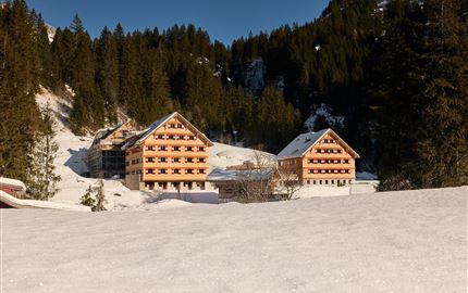 Eine Gruppe junger Menschen sitzt am Lagerfeuer und kocht über offenem Feuer. Sie lachen und genießen die Zeit in der Natur.