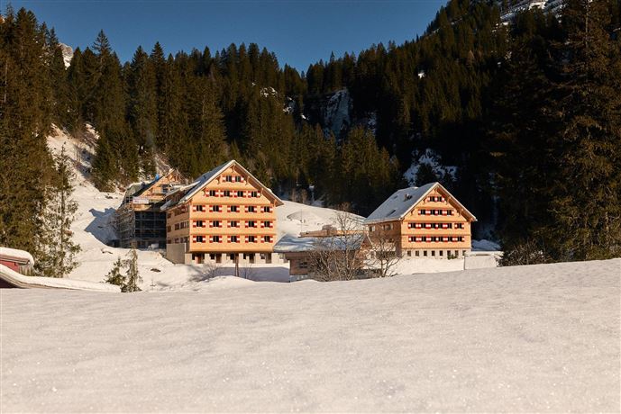 A group of young people sits by the campfire and cooks over an open fire. They laugh and enjoy their time in nature.