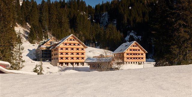 A group of young people sits by the campfire and cooks over an open fire. They laugh and enjoy their time in nature.