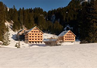 Eine Gruppe junger Menschen sitzt am Lagerfeuer und kocht über offenem Feuer. Sie lachen und genießen die Zeit in der Natur.
