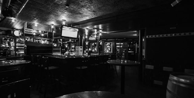 Eine dunkle Bar mit einem langen Thekenbereich und Tischen. Die Atmosphäre wirkt gemütlich und intim.
