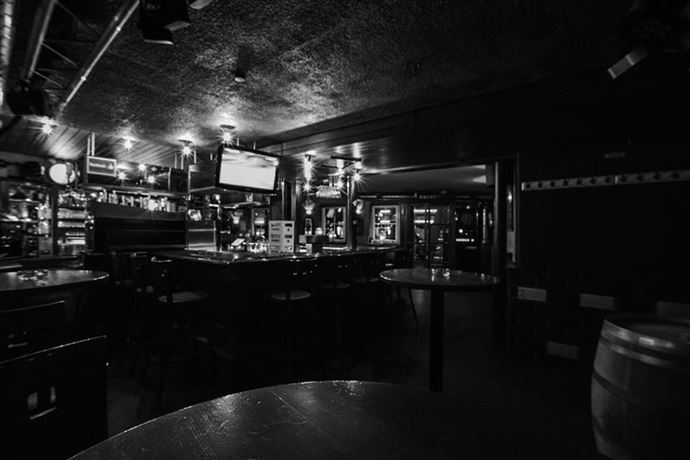 Eine gemütliche Bar mit einem dunklen Interieur und mehreren Tischen. Die Atmosphäre ist ruhig und einladend.