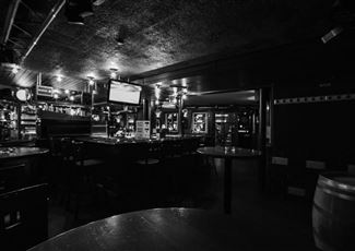 Eine gemütliche Bar mit einem dunklen Interieur und mehreren Tischen. Die Atmosphäre ist ruhig und einladend.
