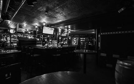 Eine dunkle Bar mit einem langen Thekenbereich und Tischen. Die Atmosphäre wirkt gemütlich und intim.