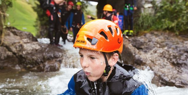 Ein Abenteuer im Wildwasser. Eine Person klettert an einem Felsen entlang, während Wasser spritzt.