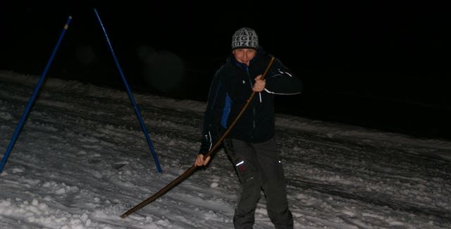 Ein Skifahrer bei Nacht auf einer schneebedeckten Piste. Er hält einen Stock in der Hand und trägt passende Ski-Ausrüstung.