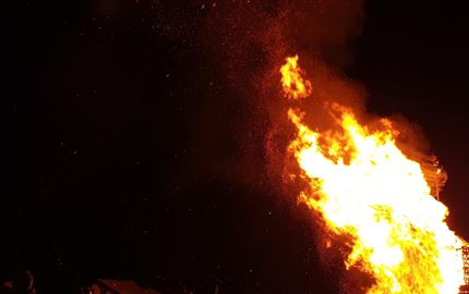 Ein loderndes Feuer erleuchtet die Nacht. Funken fliegen in die Luft und erzeugen eine dramatische Atmosphäre.