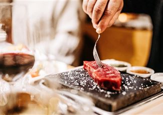 Ein saftiges Steak wird auf einem heißen Stein serviert. Der Tisch ist elegant gedeckt und es gibt verschiedene Saucen dazu.
