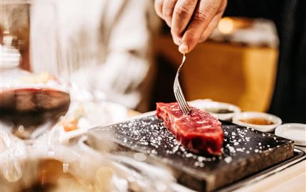 Ein saftiges Steak wird auf einem heißen Stein serviert. Der Tisch ist elegant gedeckt und es gibt verschiedene Saucen dazu.