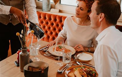Ein elegantes Abendessen mit zwei Gästen. Der Kellner serviert Wein zu einem schön gedeckten Tisch mit leckerem Essen.