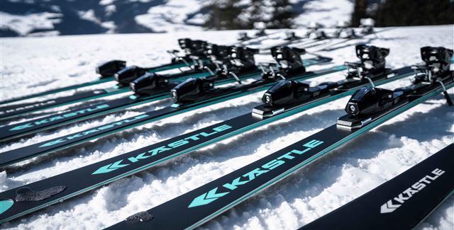 Ein Ski-Experte spricht mit einer Kundin und hält ein Paar Skier in der Hand. Im Hintergrund ist ein stylisches Sportgeschäft zu sehen.