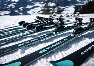 Ein Ski-Experte spricht mit einer Kundin und hält ein Paar Skier in der Hand. Im Hintergrund ist ein stylisches Sportgeschäft zu sehen.