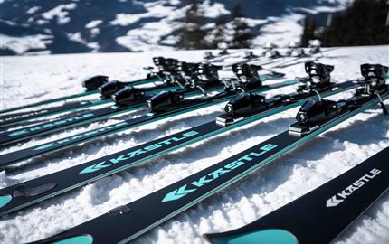 Ein Ski-Experte spricht mit einer Kundin und hält ein Paar Skier in der Hand. Im Hintergrund ist ein stylisches Sportgeschäft zu sehen.