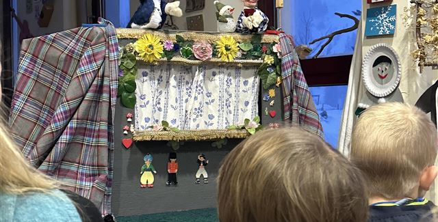 A puppet stage with colorful marionettes and a decorative backdrop. Children watch fascinated.