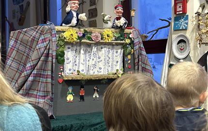 A puppet stage with colorful marionettes and a decorative backdrop. Children watch fascinated.