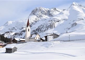 Eine verschneite Landschaft mit einem kleinen Dorf und einer Kirche. Im Hintergrund erheben sich majestätische Berge.
