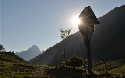 Eine idyllische Berglandschaft mit einem kleinen Baum und einer Lichtung. Die Sonne scheint hinter einem Berg hervor und beleuchtet die Szene.
