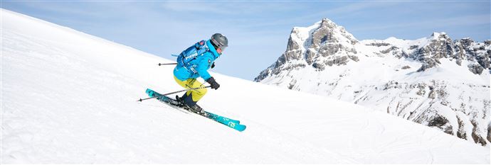 A skier is skiing on a snow-covered slope. Impressive mountains can be seen in the background.