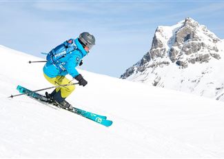 A skier is skiing on a snow-covered slope. Impressive mountains can be seen in the background.