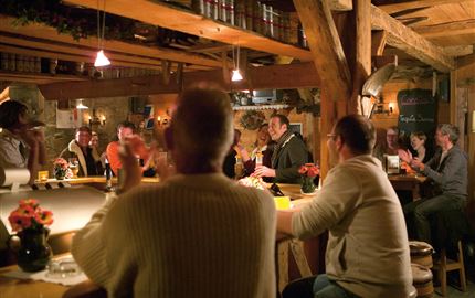 Eine gemütliche Bar mit Holzmöbeln und warmem Licht. Menschen sitzen an der Theke und haben eine gute Zeit miteinander.