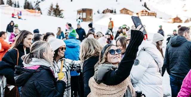 Eine lebhafte Veranstaltung in einer modernen Halle mit einer Band auf der Bühne. Die Menge jubelt und genießt die Musik.