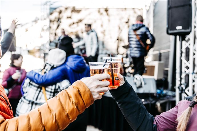 Eine Live-Band spielt auf einer Bühne in den Bergen. Im Hintergrund sind schneebedeckte Gipfel und Zuschauer, die das Konzert genießen.
