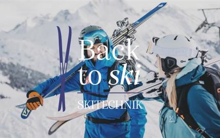 Eine Skifahrerin fährt den Hang hinunter, während eine weitere Person im Hintergrund fährt. Der Schnee ist frisch und die Landschaft wirkt winterlich.