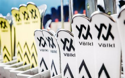 Eine Reihe von Skiern mit dem Markennamen Völkl ist ordentlich aufgereiht. Die Skier sind in verschiedenen Farben und Designs zu sehen.