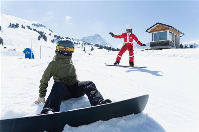 Eine Person fährt mit Skiern durch eine verschneite Landschaft. Im Hintergrund sind Berge und ein klarer blauer Himmel zu sehen.