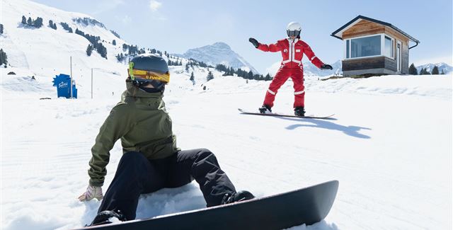 A person is skiing through a snowy landscape. In the background, mountains and a clear blue sky can be seen.