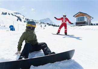 Eine Person fährt mit Skiern durch eine verschneite Landschaft. Im Hintergrund sind Berge und ein klarer blauer Himmel zu sehen.