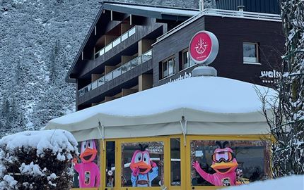 A cozy restaurant with large windows, decorated with colorful figures. The surroundings are snow-covered and surrounded by mountains.