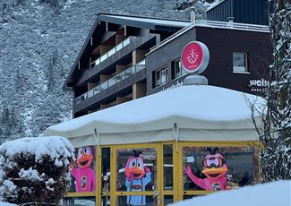 A cozy restaurant with large windows, decorated with colorful figures. The surroundings are snow-covered and surrounded by mountains.