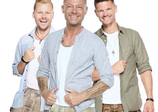 Eine Live-Band spielt auf einer Bühne in den Bergen. Im Hintergrund sind schneebedeckte Gipfel und Zuschauer, die das Konzert genießen.