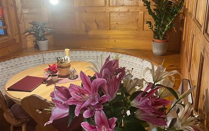 Ein gemütlicher Essbereich mit Holzvertäfelung und einem runden Tisch. Auf dem Tisch steht eine Vase mit bunten Lilien und es gibt einige Pflanzen im Hintergrund.