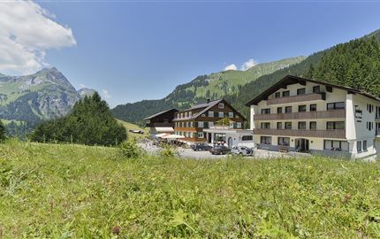 Ein malerisches Hotel in einer bergigen Landschaft. Umgeben von grünen Wiesen und majestätischen Bergen unter einem klaren blauen Himmel.