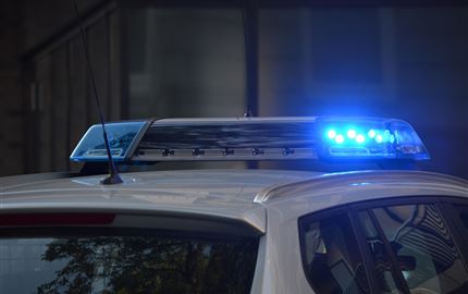 Ein Polizeiauto mit blinkenden blauen Lichtern. Der Wagen steht in einer urbanen Umgebung.