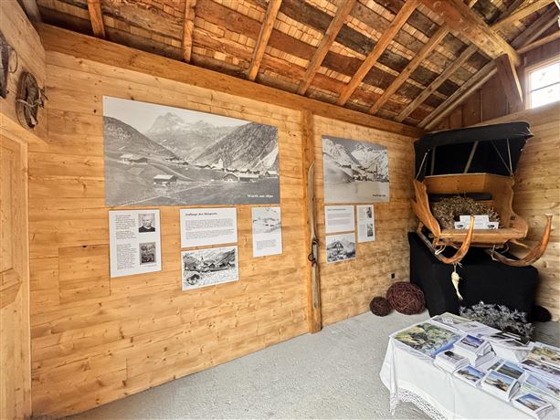 Ein traditioneller Raum mit Holzwänden und historischem Dekor. An den Wänden hängen Schwarzweißbilder und informative Tafeln über die Region.