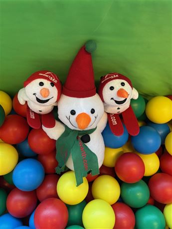 Drei fröhliche Schneemänner stehen in einem bunten Ballpool. Die farbigen Bälle sind rot, blau, gelb und grün.