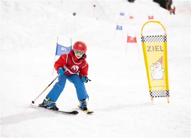 A child is skiing on a snowy slope. In the background, target markers and flags can be seen.