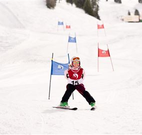 A young skier is going through a slalom course in the snow. He is wearing a red suit with the number 15 and has colorful ski equipment.
