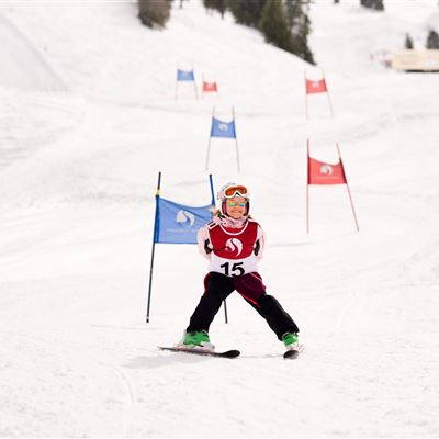 A young skier is going through a slalom course in the snow. He is wearing a red suit with the number 15 and has colorful ski equipment.