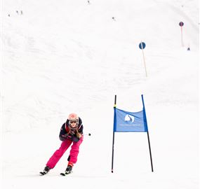 Ein Skifahrer in pinker Ausrüstung fährt auf einer verschneiten Piste. Im Hintergrund sind markierte Tore sichtbar.