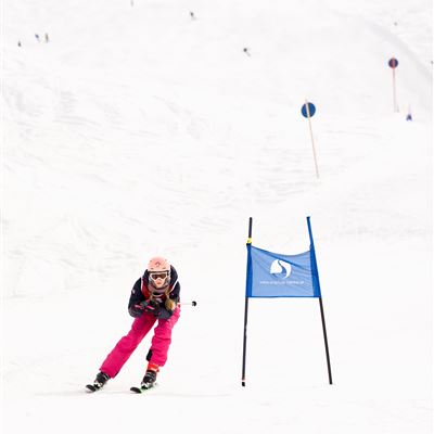 Eine Skifahrerin fährt schnell eine Piste hinunter. Im Hintergrund sind weitere Skifahrer und Schnee zu sehen.