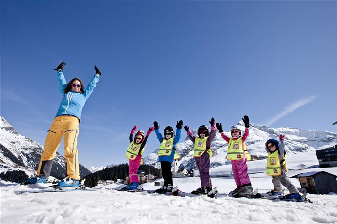 A group of skiers in colorful ski suits is skiing on a snow-covered slope. In the background, mountains and cabins can be seen, with a discount offer of 100%.