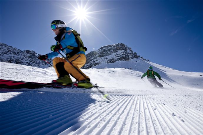 Zwei Skifahrer stehen im Schnee und lächeln sich an. Ein roter Kreis zeigt „15% Rabatt!“ an.