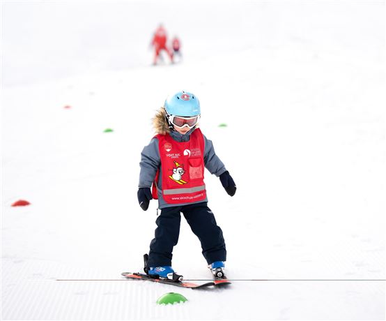 A small child is skiing on a snowy slope. They are wearing a blue helmet and a red vest.